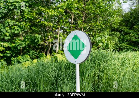 Panneau routier minimal dans un environnement verdoyant luxuriant, symbole debout parmi les hautes herbes et les arbres, zone de conservation de la nature ou route écologique, concept de en Banque D'Images