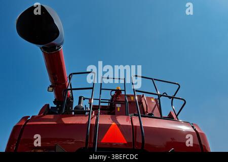 Vue arrière d'une moissonneuse-batteuse agricole rouge avec vis à grain déployée, rails de sécurité et ciel bleu vif en arrière-plan. Prise de vue à partir d'un angle bas Banque D'Images