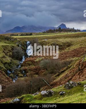 Cascade Highland coulant à travers des landes d'hiver brumeuses avec un ciel spectaculaire et un sommet de montagne lointain dans le nord rural de l'Écosse. Banque D'Images