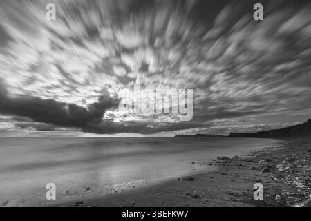 Image en noir et blanc longue exposition du ciel côtier spectaculaire au-dessus de l'île de Wight, montrant le mouvement des nuages striés et le littoral paisible. Banque D'Images