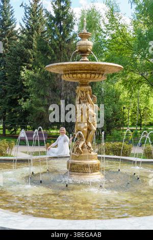 portrait urbain d'une femme d'âge moyen sur fond de fontaine. Fille vêtue d'une robe blanche. Banque D'Images