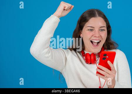 Excité jeune femme célébrant tout en regardant smartphone Banque D'Images