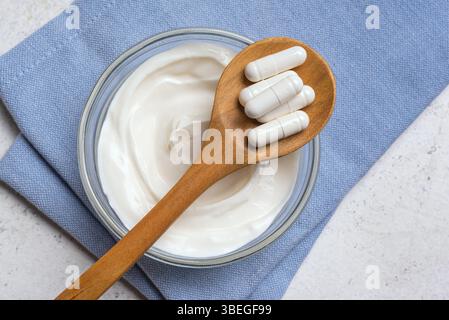 Capsules probiotiques sur cuillère en bois et bol de kéfir ou yogourt. Aliments fermentés, supplément nutritionnel, régime alimentaire sain pour le concept de digestion. Banque D'Images
