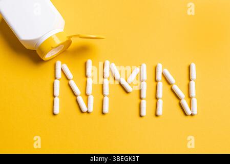 Supplément de nicotinamide mononucléotide, niacine, vitamine anti-âge. Pilules blanches formant forme aux lettres NMN sur fond jaune, espace copie, top vi Banque D'Images