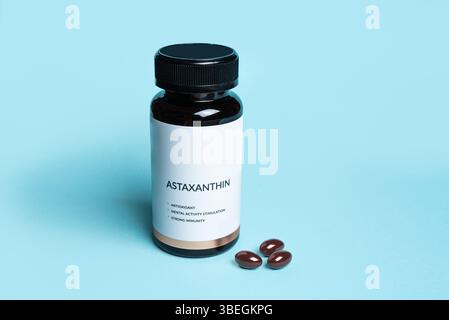 Supplément d'astaxanthine en bouteille avec étiquette vierge sur fond bleu, espace de copie. Mode de vie sain, supplément diététique antioxydant. Banque D'Images