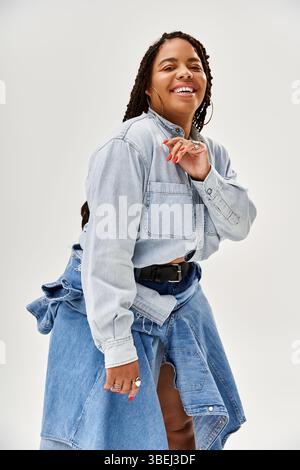 Une joyeuse femme afro-américaine en tresses et en denim rayonne de bonheur. Banque D'Images