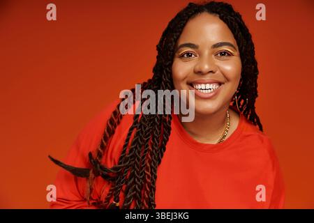 Une femme afro-américaine joyeuse dans une tenue élégante rayonne de positivité sur un fond orange. Banque D'Images