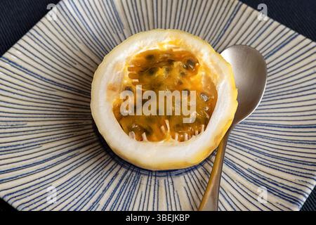 Fruit de la passion coupé en deux montrant sa pulpe dorée remplie de graines scintillantes serties sur une plaque de céramique avec un motif bleu radial dirigeant l'œil Banque D'Images
