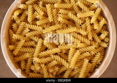 Pâtes fusilli non cuites dans un grand bol en bois, un ingrédient sec de base dans la cuisine méditerranéenne connue pour sa forme en spirale et sa polyvalence dans la cuisine Banque D'Images