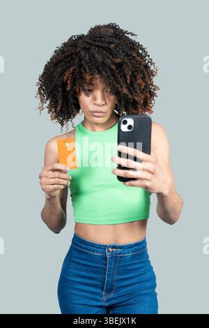 La jeune femme utilise son smartphone et sa carte de crédit pour faire des achats en ligne sur un fond gris Banque D'Images