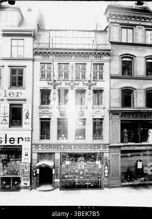 Cette photographie, prise par Peter Elfelt, montre Cornelius Knudsen au Købmagergade 15 à Copenhague, Danemark. L'image remonte au début du XXe siècle et souligne le caractère historique de la rue. Banque D'Images