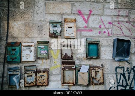Gros plan d'un mur en pierre altérée orné d'une collection de boîtes aux lettres vintage. Les boîtes aux lettres, dans divers états de délabrement, affichent un Pat Banque D'Images