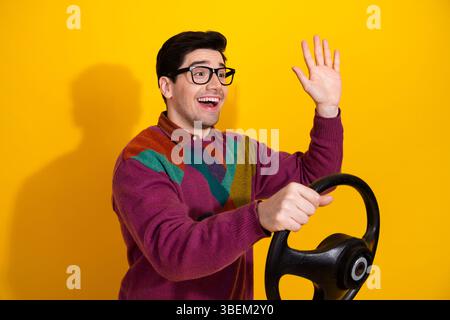 Jeune homme avec des gestes d'expression joyeux tout en faisant semblant de conduire, portant un pull décontracté style rétro Banque D'Images