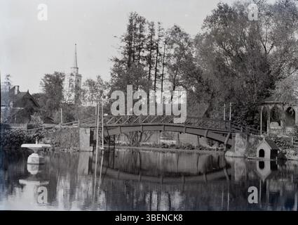 Photographie prise entre 1900 et 1910 montrant le jardin de la Société des artisans allemands à Tartu, comprenant un étang et un pont en bois. Banque D'Images