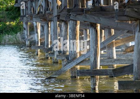 Un charmant pont piétonnier en bois s'étend sur la rivière, ses planches altérées offrant un chemin rustique à travers la nature. Le flux serein du ri Banque D'Images