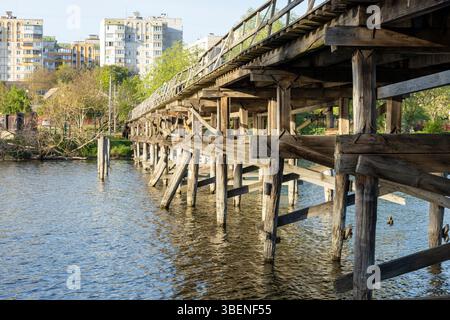Un charmant pont piétonnier en bois s'étend sur la rivière, ses planches altérées offrant un chemin rustique à travers la nature. Le flux serein du ri Banque D'Images
