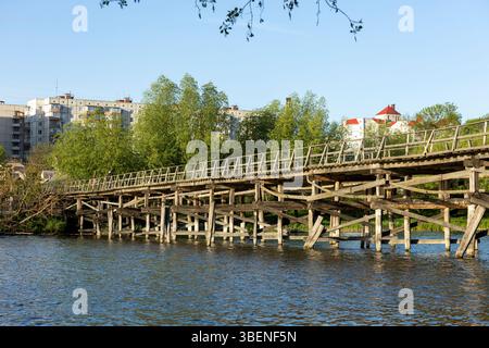 Un charmant pont piétonnier en bois s'étend sur la rivière, ses planches altérées offrant un chemin rustique à travers la nature. Le flux serein du ri Banque D'Images