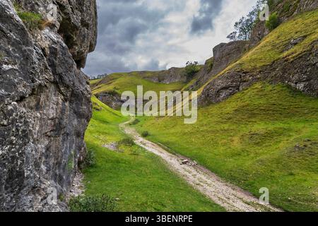 Le sentier de gravier sinueux qui traverse le centre de la gorge calcaire de Cave Dale à Castleton, Peak District, avec un ciel spectaculaire. Banque D'Images