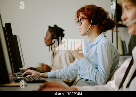 Groupe diversifié d'agents de centre d'appels travaillant avec diligence à leur bureau, communiquant avec les clients via des micro-casques et des ordinateurs. S'engager dans la profession Banque D'Images