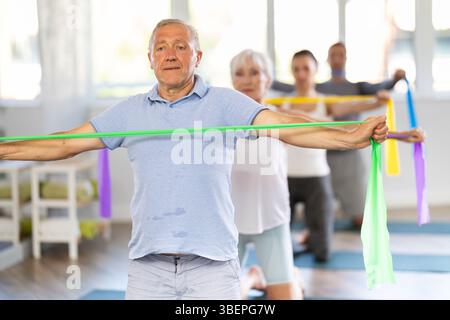 Groupe de personnes matures faisant des exercices d'étirement des bras en utilisant des bandes de résistance tout en s'agenouillant sur des tapis Banque D'Images