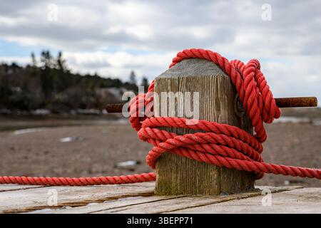 Corde rouge attachée autour d'un poteau sur un quai en bois. Marée basse, plage en arrière-plan. Ciel couvert. Banque D'Images