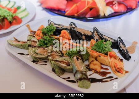Présentation élégante d'un plateau de sushis avec divers rouleaux, y compris ceux avec des moules noires, de l'avocat et du thon rouge vif, orné de g balsamique Banque D'Images