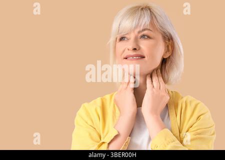 Femme mature auto-examinant la glande thyroïde sur fond beige, gros plan Banque D'Images