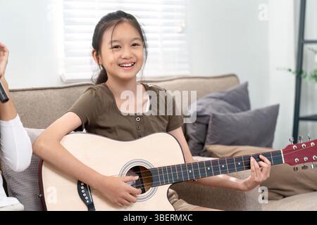 Musique joyeuse et connexion familiale. Une fille souriante en jouant de la guitare, profitant d'un moment avec sa mère. Banque D'Images