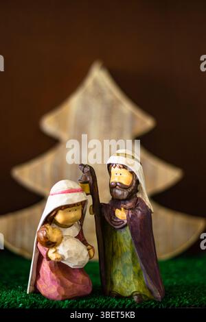 Figures de style enfant de la Sainte famille avec un arbre de Noël en bois en arrière-plan Banque D'Images