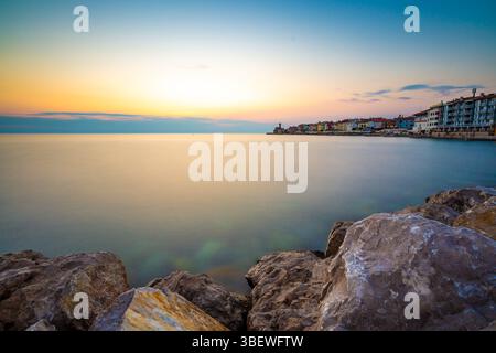 Coucher de soleil au-dessus de la mer adriatique dans la ville de Piran, Slovénie. Vieille ville ancienne et médiavée, vue de la côte et du port. Vieilles pierres en premier plan, belles Banque D'Images