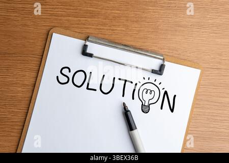Une vue de haut en bas montre un presse-papiers avec un mot « SOLUTION » et un stylo sur une table en bois. Banque D'Images