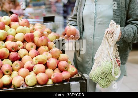 Femme méconnaissable sélectionnant des pommes fraîches dans la section des produits du marché, en utilisant un sac en maille écologique pour acheter des fruits et des légumes Banque D'Images