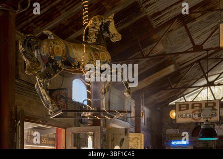 Un cheval de carrousel vieilli avec des lumières de fées est suspendu au plafond d'un bar sud-africain à thème vintage avec des signes nostalgiques et un toit rustique. Banque D'Images