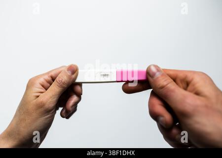 Gros plan de deux mains, un homme et une femme, tenant ensemble un test de grossesse positif, symbolisant l'excitation partagée et l'unité émotionnelle au début Banque D'Images