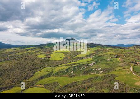 Vue imprenable sur les collines vallonnées de Toscane sous un ciel nuageux. Des champs verdoyants et une ville historique perchée créent un paysage pittoresque, idéal Banque D'Images