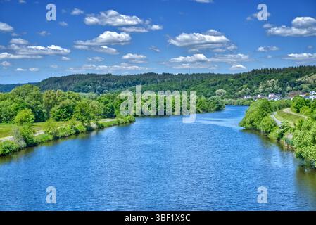 La rivière saar coule gracieusement à travers un paysage pittoresque, entouré d'arbres verts vibrants et d'un ciel bleu clair parsemé de nuages blancs moelleux Banque D'Images