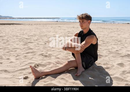 Jeune athlète assis sur le sable à la plage Banque D'Images