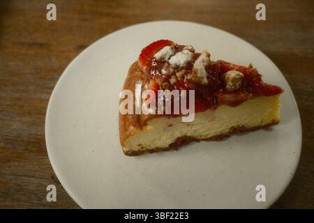 Une tranche de cheesecake crémeux garnie de fraises fraîches, de sucre en poudre et de crumble croustillant Banque D'Images