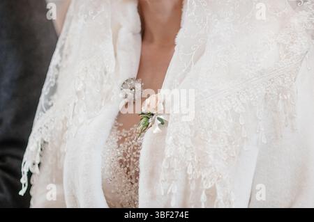 Un plan détaillé se concentre sur le haut de la poitrine d'une mariée portant une délicate veste de mariage en dentelle blanche, accentuée d'une broche étincelante et d'un seul blus Banque D'Images