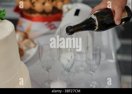 Un gros plan montre une personne versant du champagne pétillant d'une bouteille sombre dans plusieurs verres clairs, symbolisant une occasion joyeuse comme un mariage Banque D'Images
