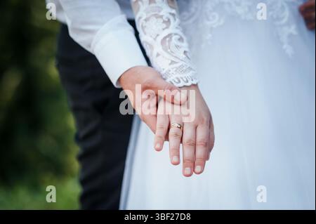 Une image détaillée se concentre sur les mains d'une mariée et mariée, mettant en valeur leurs alliances comme ils se tiennent ensemble, représentant une union aimante dans la nature Banque D'Images