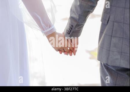 Moment intime d'une mariée et mariée marchant ensemble, les mains attachées dans l'affection lors d'une cérémonie de mariage de jour lumineux, tissu doux et transparent de la w Banque D'Images