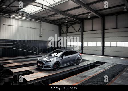Ford Focus ST berline dans un garage vide. Vue aérienne de trois quarts de face de la voiture grise garée dans un entrepôt vide - station d'entretien d'autobus avec fosse de véhicule. Banque D'Images