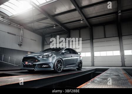 Ford Focus ST gris dans un garage vide. Vue de trois quarts avant grand angle de la berline garée dans un entrepôt vide - station d'entretien d'autobus avec fosse de véhicule. Banque D'Images