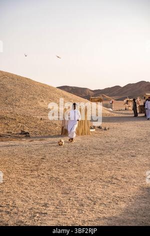Le Caire, Egypte - 11 septembre 2023 : homme habillé en tenue traditionnelle profitant d'un match de football au milieu d'un paysage désertique serein en Egypte. Banque D'Images