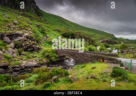 Un magnifique pont de voeux en pierre pittoresque est élégamment niché au milieu de la verdure vibrante de Gap of Dunloe, et du ciel dramatique et sombre, le tout à l'intérieur d'un se Banque D'Images