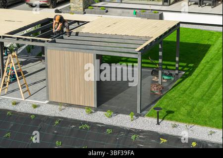 Un travailleur construit soigneusement le toit d'un pavillon extérieur élégant dans une cour verte. Les outils à proximité indiquent les efforts continus d'amélioration de la maison. Banque D'Images