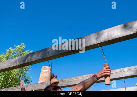 Homme athlétique faisant un exercice de pull up sur un parcours d'obstacles en bois extérieur, course spartiate de compétition OCR Banque D'Images