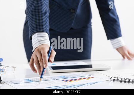 Femme d'affaires debout près du bureau et analysant les graphiques financiers. Directeur d'entreprise réussi dans le costume d'affaires. Gros plan main de femme avec stylo. B Banque D'Images
