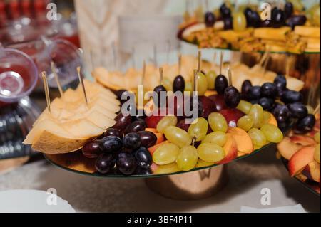 Un plateau de fruits magnifiquement arrangé avec cantaloup, raisins rouges et verts sur des supports en verre à gradins offre une sélection alléchante pour une fête ou même Banque D'Images